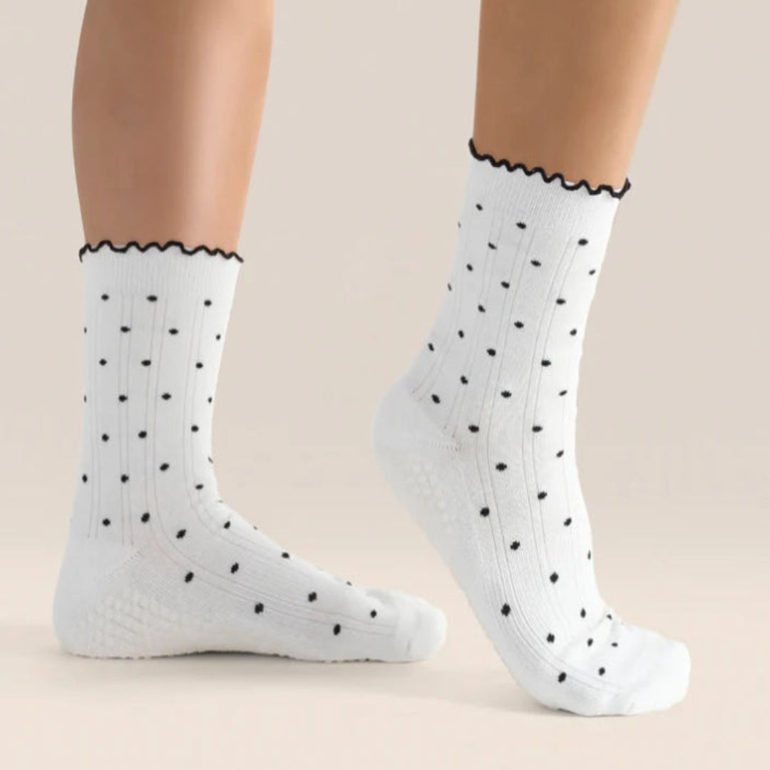 White crew socks with black polka dots worn by a person on a beige background