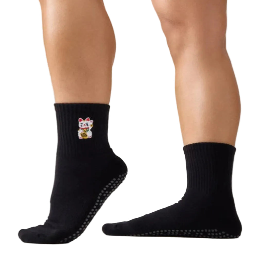 Black socks with a fortune kitty on one foot against a neutral background