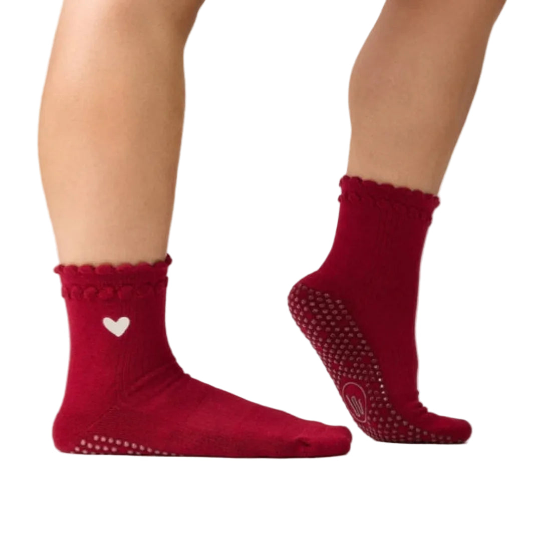 Red socks with a heart design and textured sole on a neutral background